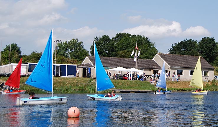 View of Otley SC clubhouse from the water on a sunny day with boats in front of it.