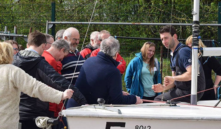 Instructor sat on a dinghy on shore chatting to a group of people on a training course.