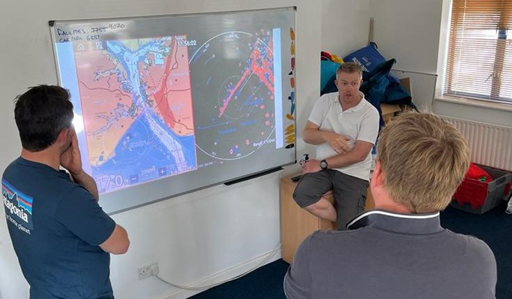 Trainer explaining a radar map on a wall screen to two delegates in a classroom for RYA Radar Course.