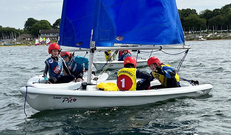 Three dinghies with junior sailors in OnBoard bibs and helmets having fun as part of the Rookie Fleet powered by OnBoard at the 2023 BYS Midlands Regional Junior Championships at Rutland SC.