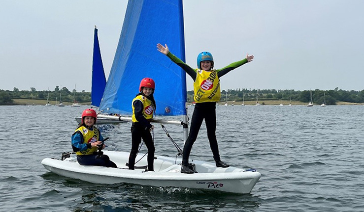 Two Fusion dinghies on a sunny day each with two youth sailors on board, one helming, one crewing, wearing helmets.