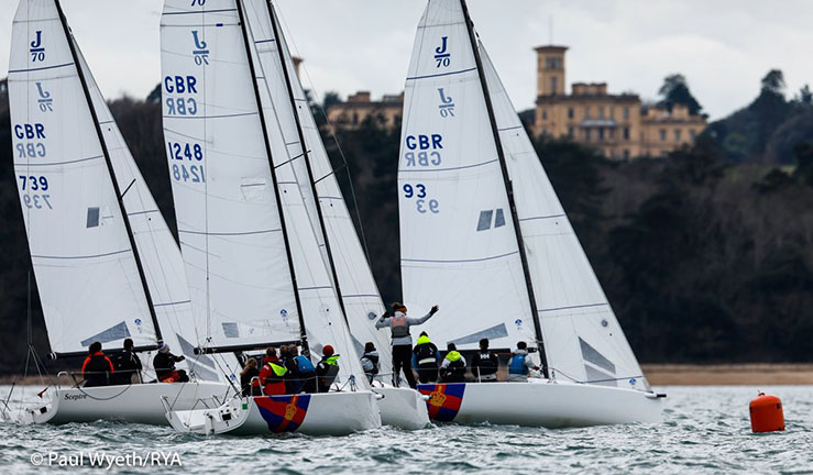 Coaches in a blue RIB alongside a fleet of J70 keelboats being sailed downwind by British Keelboat Academy recruits with blue spinnakers flying.