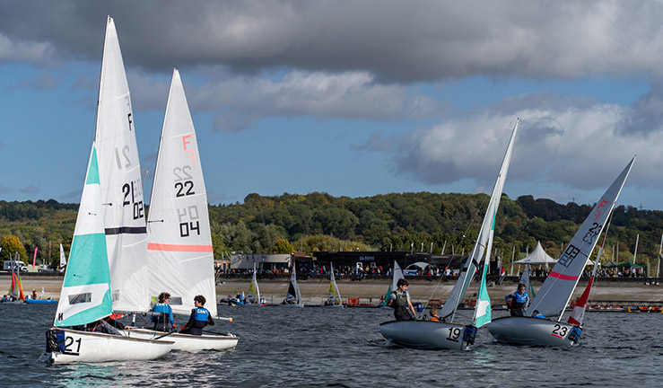 Eric Twiname Youth & Junior Team Racing Championships 2022 with four Firefly dinghies racing upwind in the foreground and Oxford Sailing Club and spectators in the background.