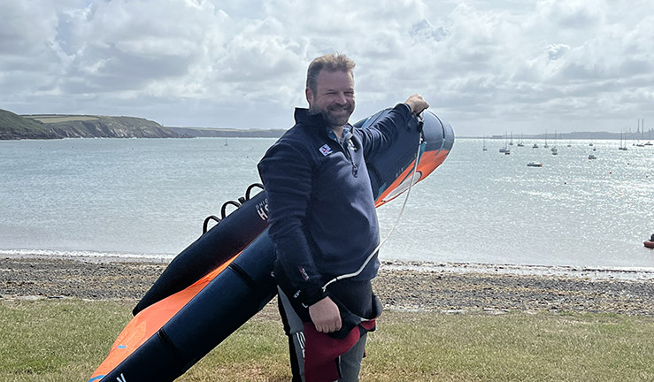 RYA Cymru Wales CEO James Stuart smiling on shore holding up a wing with the sea in the background.