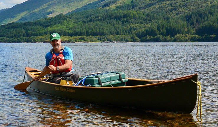 Adventurer and guiding expert Myles Farnbank in a selfie picture on the water in a ravine with two kayakers in the background.