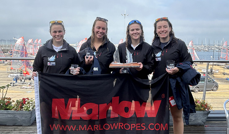 Winning team from the RYA Marlow Ropes Women's Match Racing Championship 2023, Skipper Sophie Otter flanked by team mates Amy Sparks, Hebe Hemming and Hatty Ward, holding up trophies and Marlow flag on balcony at WPNSA.