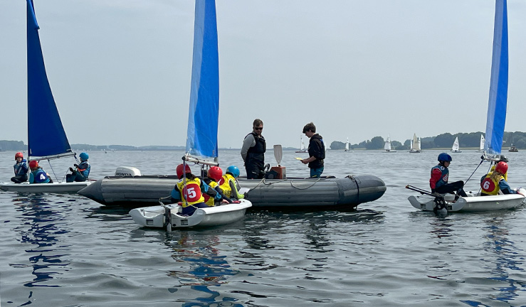 A grey RIB with two instructors surrounded by three dinghies with blue sails each with some young OnBoard sailors onboard.
