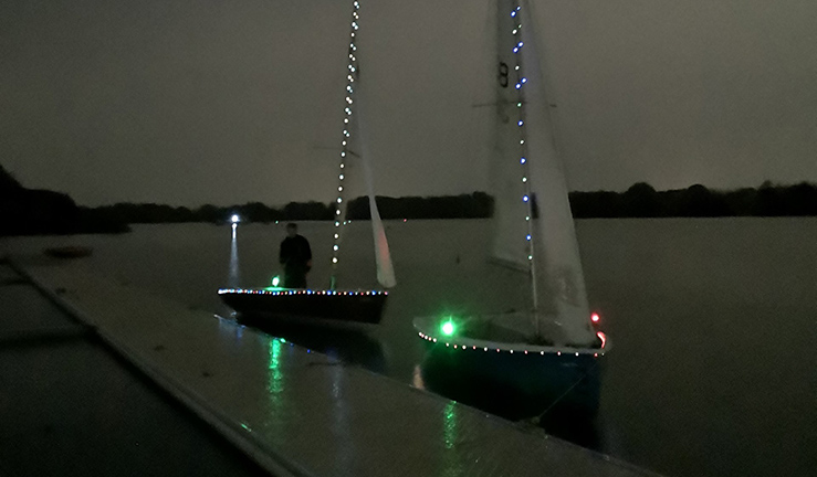 Two sailing dinghies in the dark on a pontoon at Swarkestone SC, lit up with fairy lights around the deck and up the masts for a memorable night sail for the children attending the last junior session of the season.