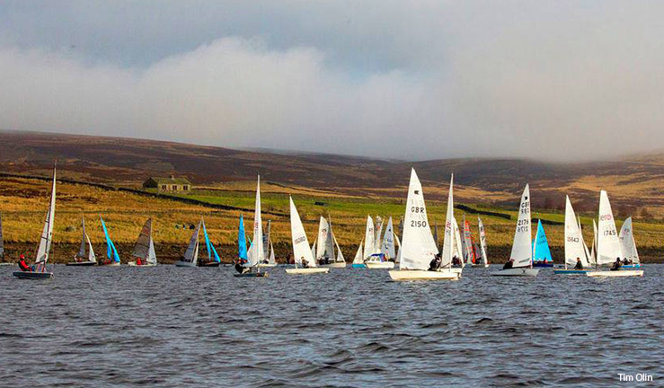 Fleet of 30 dinghies of all kinds on the water at Yorkshire Dales SC with the moors in the background and sunshine on the sails on a winter's day for the Brass Monkey.