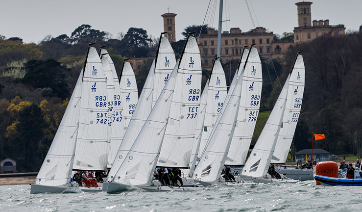 Fleet of J70s coming off a startline as part of a British Keelboat Academy exercise during a training weekend off Cowes with Osborne House on the shoreline.