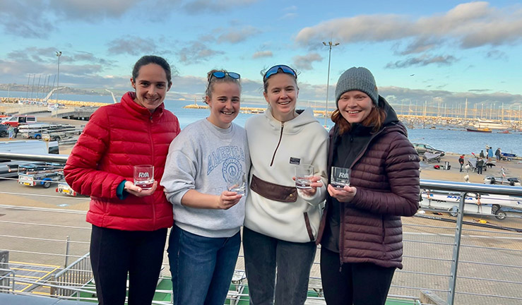 RYA/BUSA Women's Winter Match Racing champions(left to right) Verity Hopkins, Sarah Jarman, Hebe Hemming & Rosie Povall, on the balcony at WPNSA with the boatpark and blue sky in the background, each holding a winner's glass.