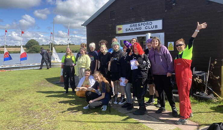 Group of a dozen smiling visitors from the Pride Youth Games outside the clubhouse at Gresford Sailing Club